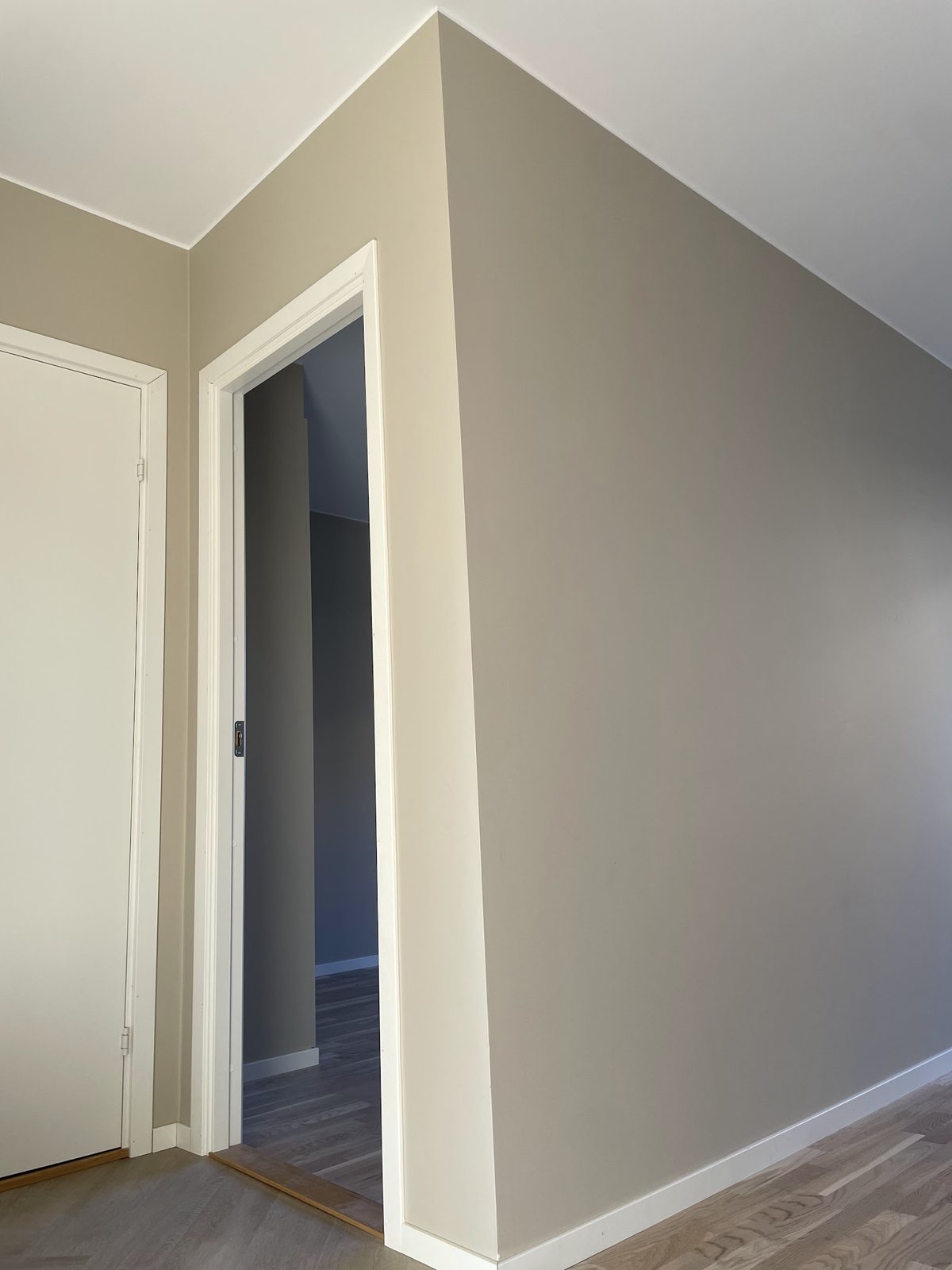 Hall med gråbeige väggar och vita dörrkarmar